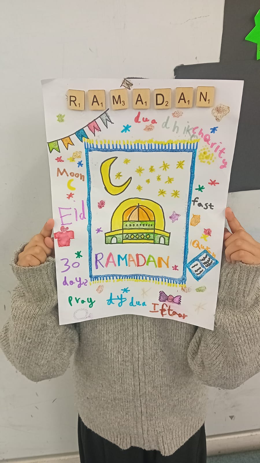 A child holding a colourful Ramadan poster made at the Madrasah